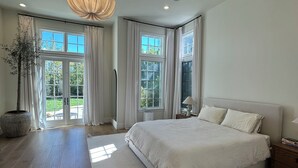 Une chambre avec un grand lit, une plante en pot et une vue sur l’extérieur.