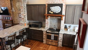 A kitchen with a brick wall, wooden cabinets, a microwave, an oven, and a bar area with stools.