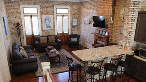 A spacious living room with a sofa, a coffee table, and a TV. There is a kitchen area with a bar and stools.