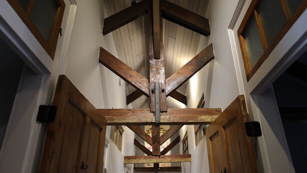 A corridor with wooden beams, white walls, and doors with glass panels.
