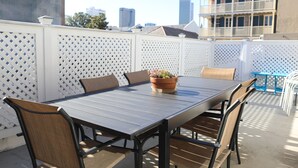 A rooftop patio with a table and chairs, a potted plant, and a view of buildings.