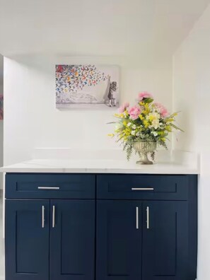 A kitchen with dark blue cabinets, a white countertop, and a floral arrangement on the counter.