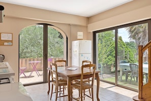 Un comedor con una mesa, sillas, un refrigerador y vistas al exterior.