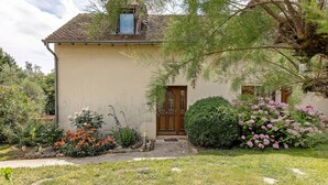 A single-story building with a brown door, a small window, and a garden with various plants and flowers.