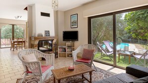 A spacious living area with wicker furniture, a fireplace, a TV, and a view of a swimming pool.