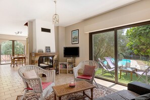 Amplia sala de estar con muebles de mimbre, chimenea, televisor y vista a una piscina.