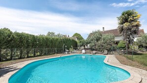 A swimming pool with a curved edge, surrounded by a fence and trees.