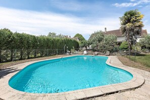 Una piscina con borde curvo, rodeada por una cerca y árboles.