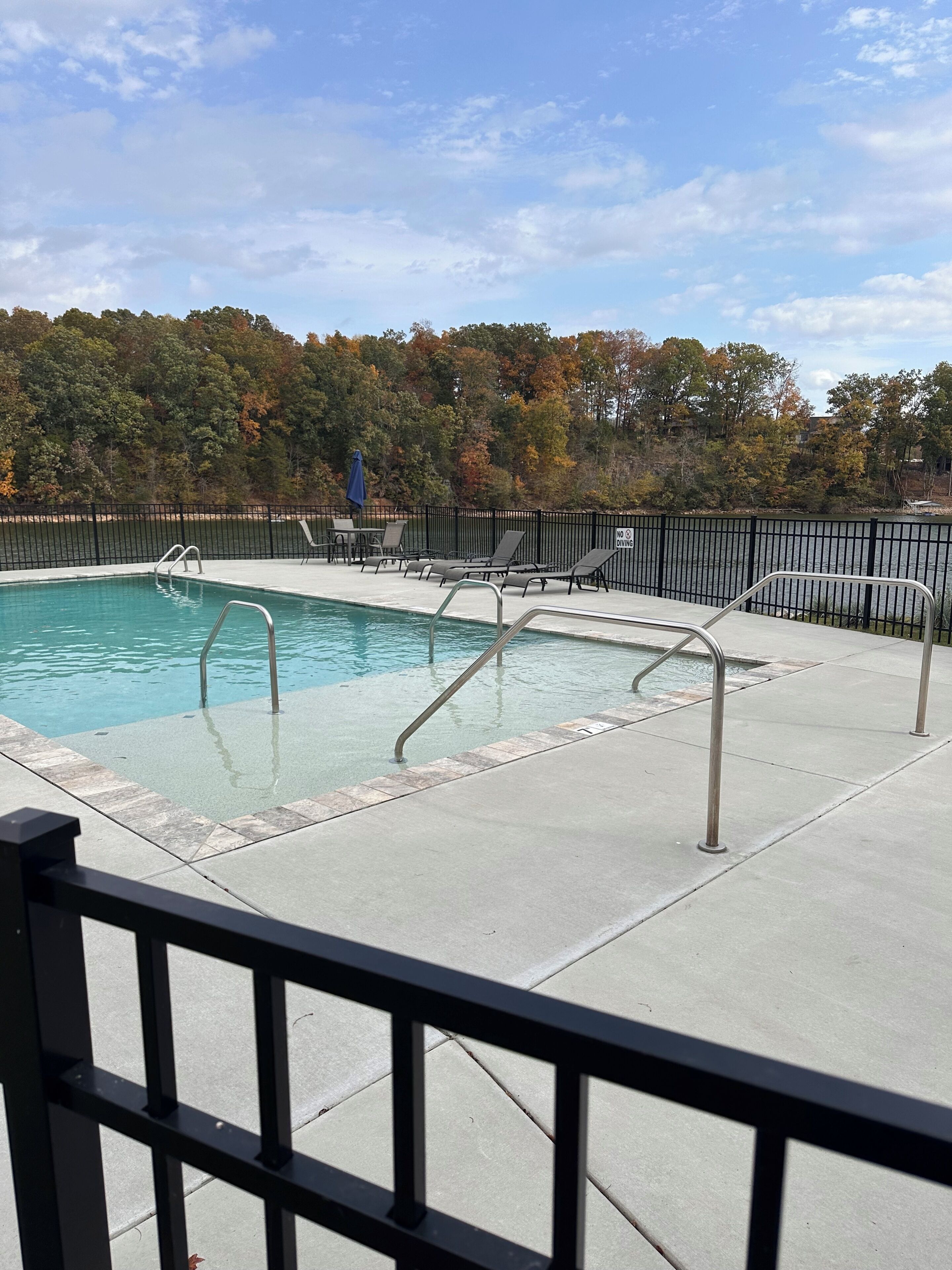 A swimming pool with a metal ladder, lounge chairs, and a fence.