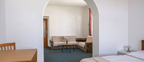 Una habitación con una mesa de madera, un sofá, una cama y un arco que da a otra habitación.