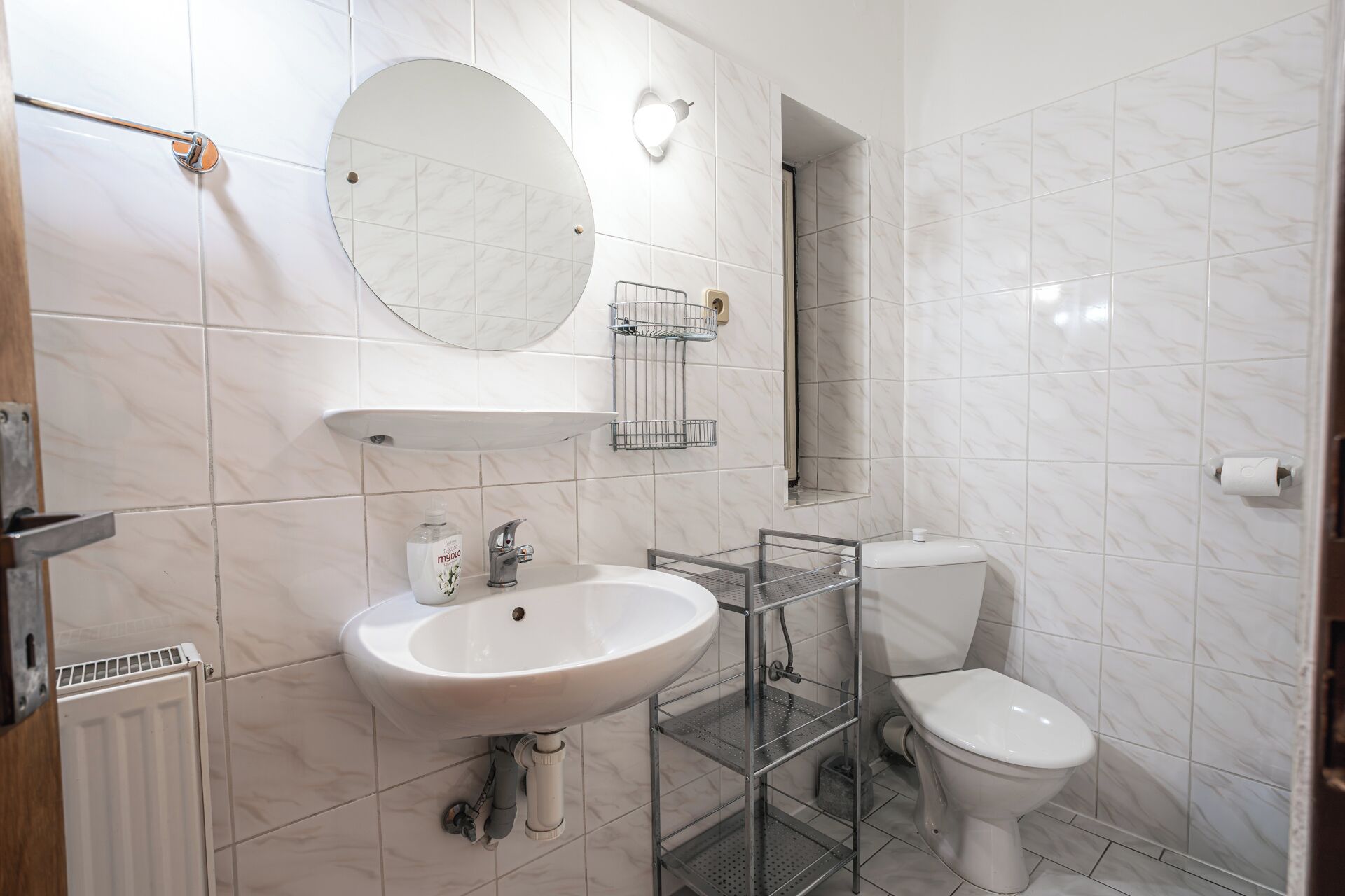 Un baño con lavamanos blanco, espejo redondo, inodoro y zona de ducha.