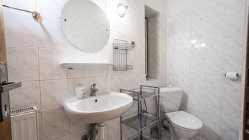 Un baño con lavamanos blanco, espejo redondo, inodoro y zona de ducha.