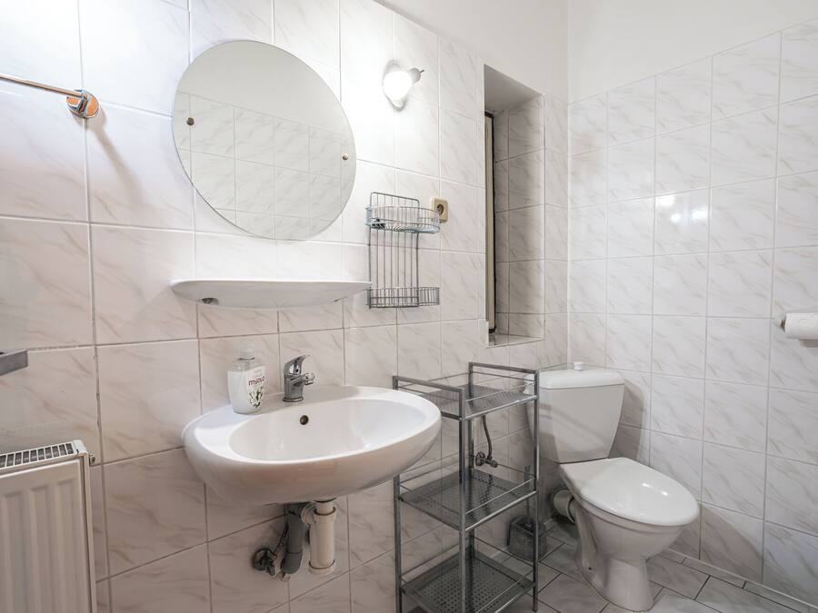 A bathroom with a white sink, round mirror, toilet, and a shower area.