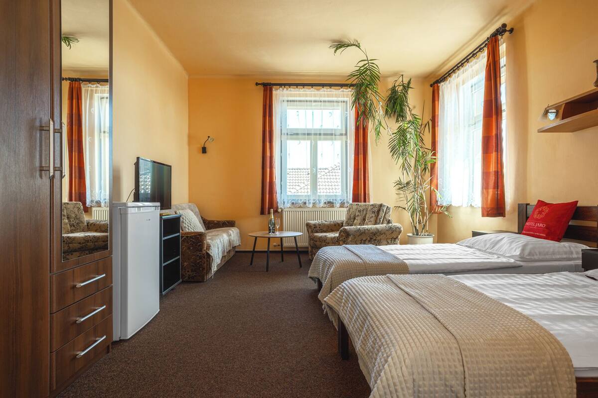 Ein Hotelzimmer mit Sofa, Bett, Schreibtisch, Fernseher und einer Zimmerpflanze.