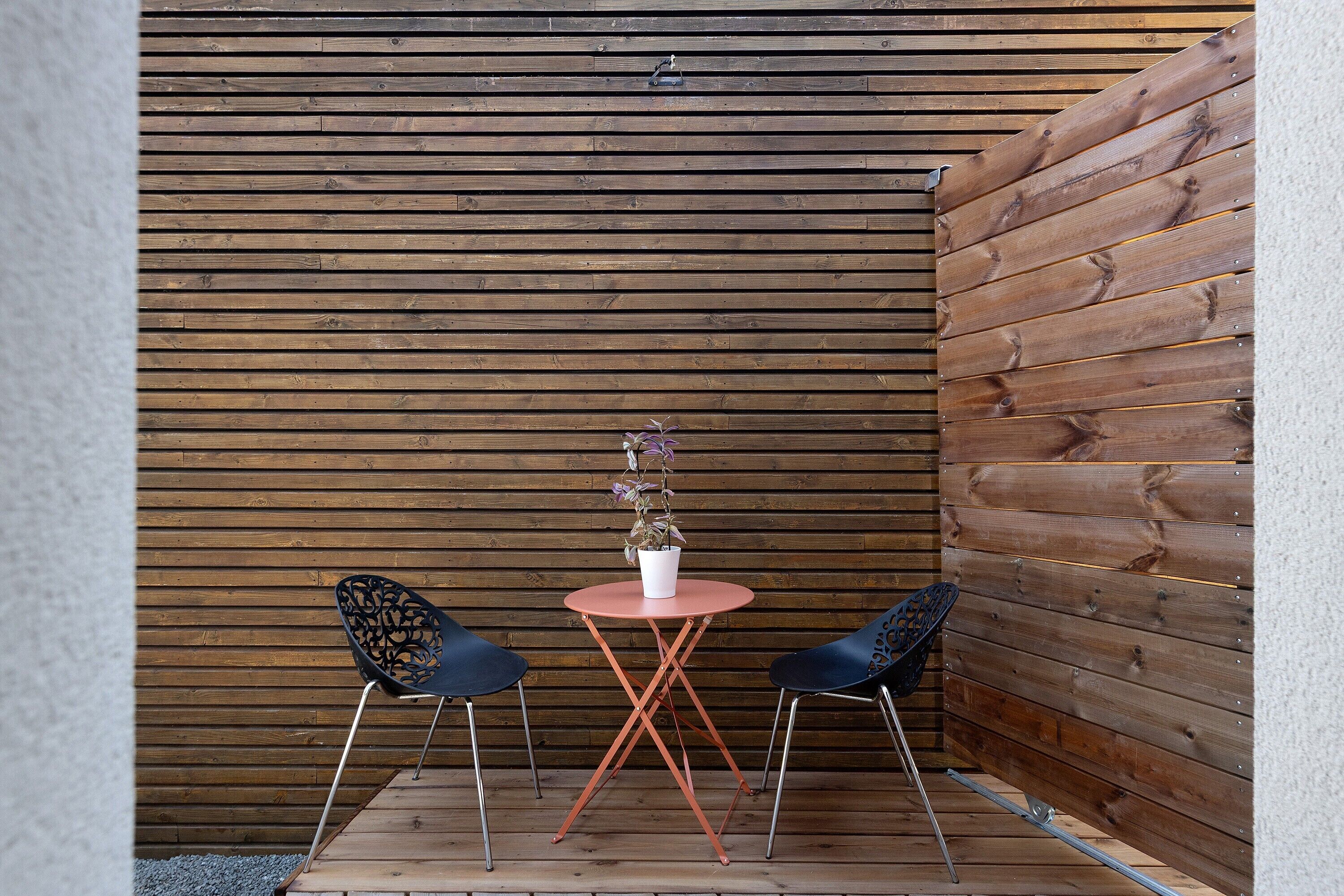 A small outdoor seating area with two chairs and a table, set against a wooden wall.