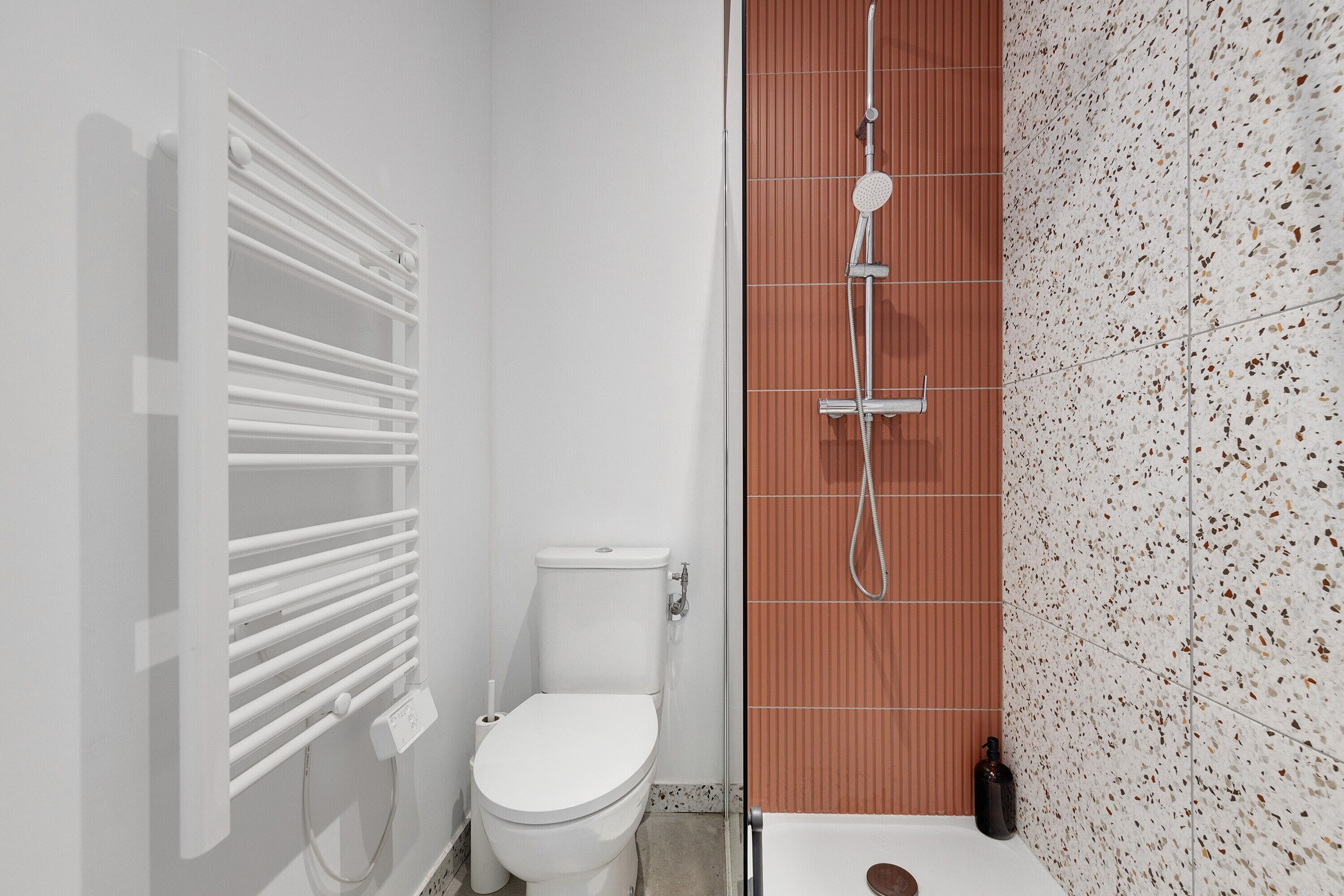 A bathroom with a white toilet, a shower with a rain showerhead, and a wall with a speckled tile pattern.