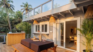 Una terraza de madera con una mesa, bancos, una barra de madera y un vidrio que da a un comedor.