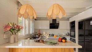 Una cocina moderna con armarios blancos, una isla grande y lámparas colgantes de ratán.