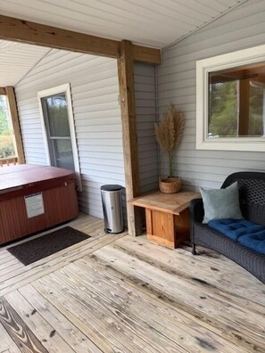 Une véranda abritée avec un jacuzzi, une poubelle, une petite table en bois et un panier en osier contenant des plumes d’herbe des pampas.