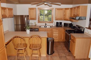 A kitchen with wooden cabinets, a stainless steel refrigerator, a microwave, a stove, and two wooden chairs. - Sialang- Private Waterfront Pier, Hot Tub, Kayaks (Chincoteague Island)