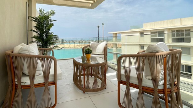 A balcony with wicker furniture, a glass table, and a view of a beach and buildings. - 2 BR Sapphire 405 in Marassi North Coast (El Alamein)
