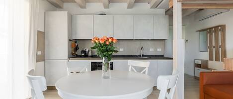 Una cocina moderna con armarios blancos, una mesa redonda de comedor con sillas blancas y un florero con flores.