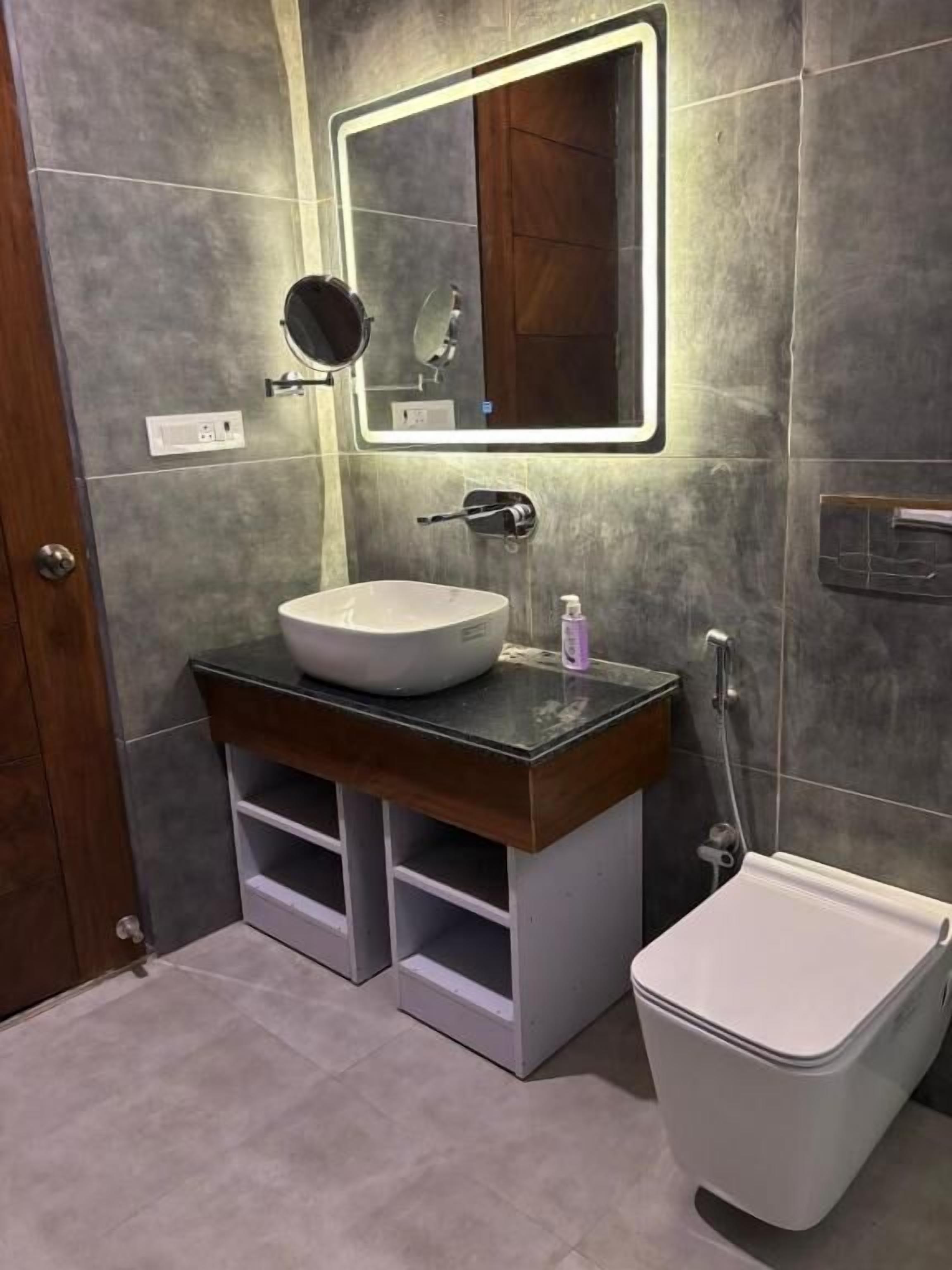 Ein Badezimmer mit rundem Spiegel, einem Aufsatzwaschbecken, Toilette und Dusche.