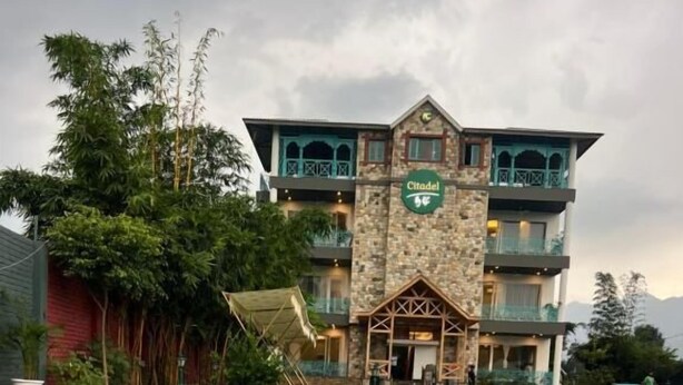 A hotel with a pool, stone facade, and balconies. - Mastiff Citadel RC (Vikasnagar)