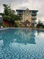 Et hotel med pool, stenfacade og altaner.