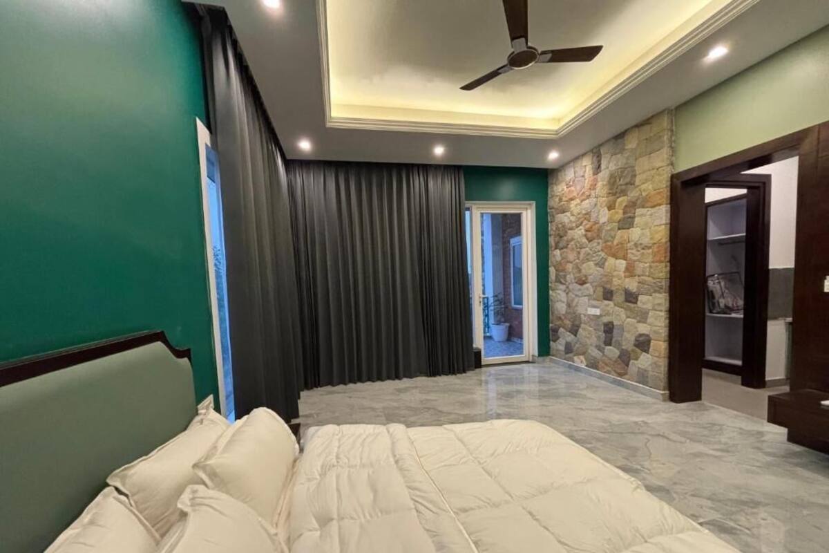 Une chambre à coucher avec un lit, un ventilateur de plafond, un mur en pierre et une porte donnant sur une autre pièce.