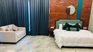 A hotel room with a bed, a sofa, a mirror, and a brick wall. - Mastiff Citadel RC (Vikasnagar)