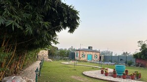 A courtyard with a stone pathway, a small building with a blue door, and potted plants. - Mastiff Citadel RC (Vikasnagar)