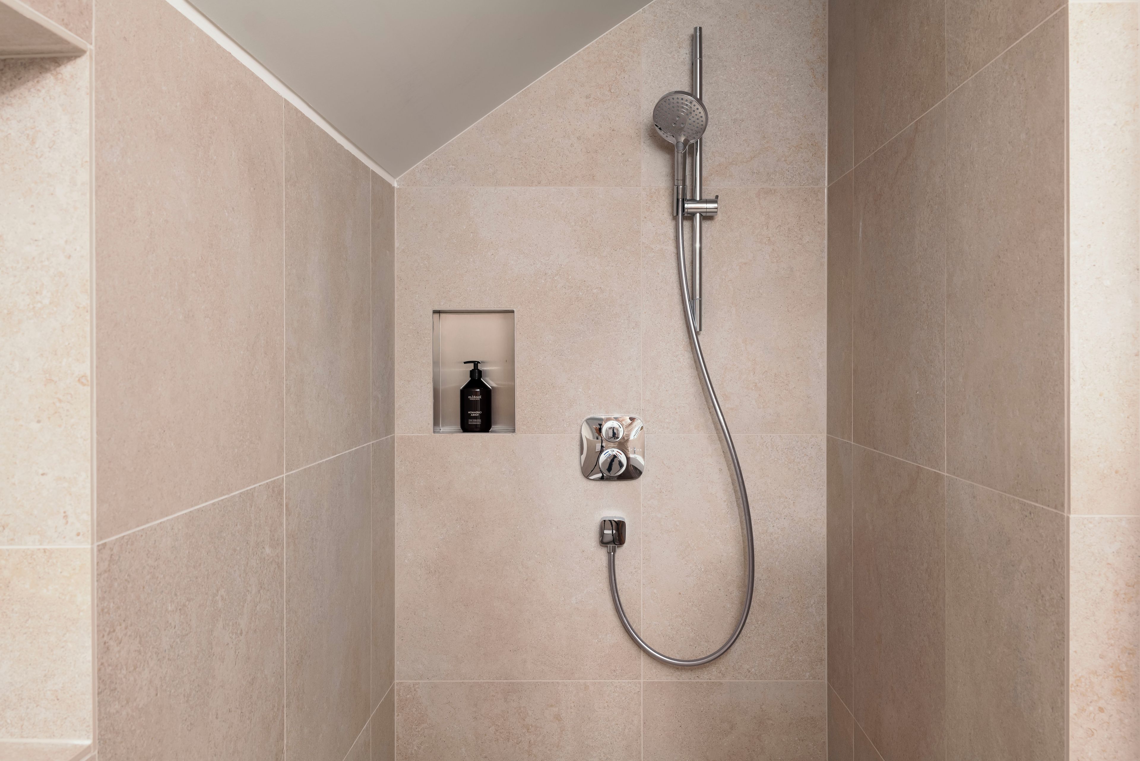 A modern shower with a handheld showerhead and a wall-mounted faucet, a soap dispenser, and a handheld showerhead.
