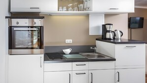 A modern kitchen with white cabinetry, a built-in oven, a stovetop, and a coffee maker. - Central Suite IV (Greifswald)