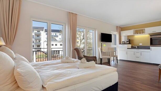 A hotel room with a bed, a desk, a chair, a TV, and a kitchen area. - Central Suite IV (Greifswald)