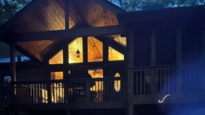 Una terraza de madera con un pozo de fuego, una silla y un edificio con ventanas iluminadas.