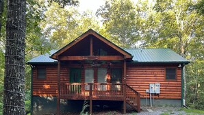 Una cabaña de troncos con un porche, un cartel que dice 'Welcome' y un cartel que indica 'Cabin'.