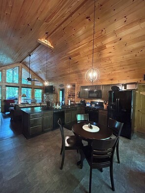 Eine geräumige Küche mit Holzbalkendecke, großen Fenstern und einem Essbereich mit rundem Tisch und Stühlen.