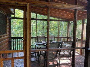 Eine Holzterrasse mit Tisch und Stühlen, umgeben von Glasgeländern, mit Blick auf eine bewaldete Landschaft.
