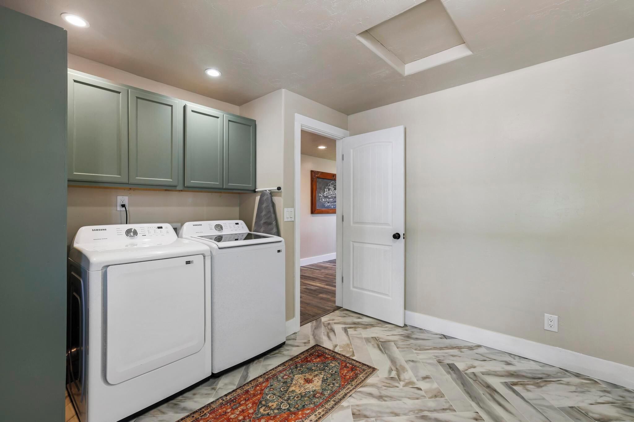 A laundry area with two white washing machines, a green cabinet, and a patterned rug.