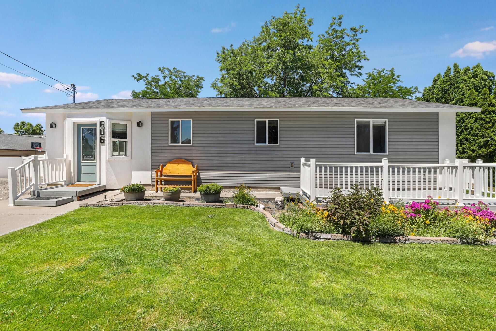 A single-story house with a front porch, a small garden, and a white fence.