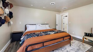 A bedroom with a bed, a nightstand, a wall-mounted hat rack, a door, and a chair.