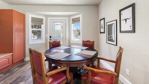 A dining room with a round table, six chairs, and a view through a door.