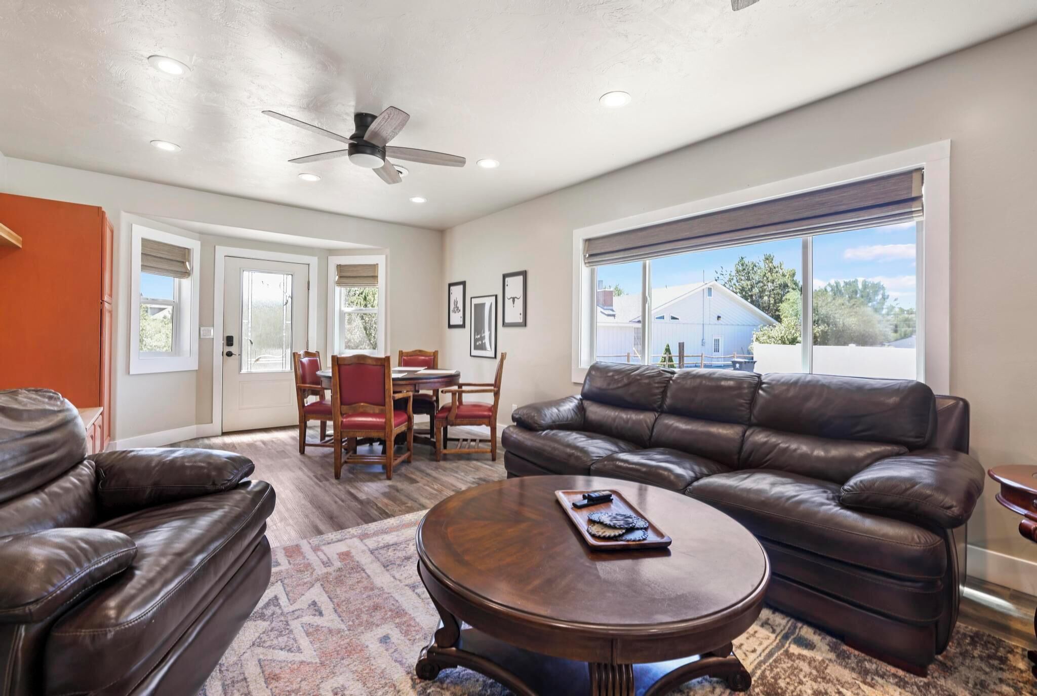 A living room with a brown leather couch, a wooden coffee table, and a dining area with chairs and a table.