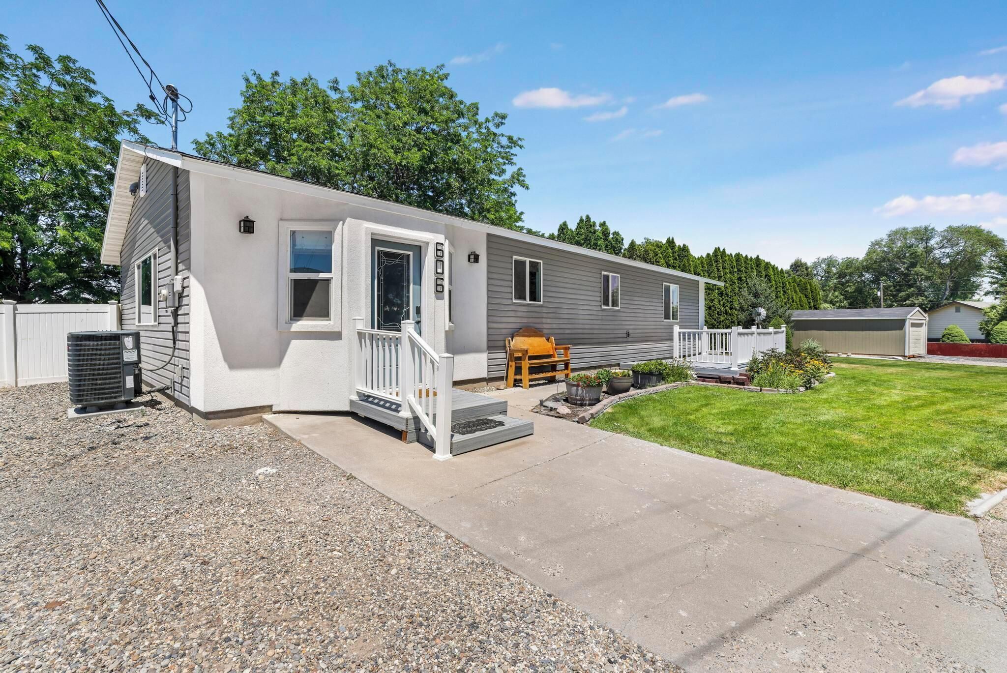 A single-story mobile home with a front porch, a small deck, and a gravel driveway.