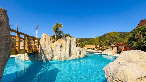 Una piscina con formaciones rocosas, un puente de madera y un cielo azul despejado.