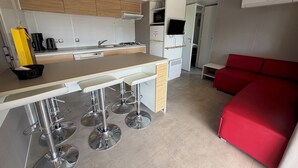 Una cocina moderna con una isla central, taburetes de bar, un sofá rojo y un televisor montado en la pared.