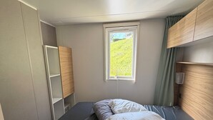 Una cama individual con colchón oscuro, dos almohadas, una ventana con vistas a la vegetación y muebles de madera.