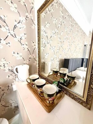 A bathroom with floral wallpaper, a mirror with an ornate frame, and a tray with cups and a kettle. - The Carlton Hotel (Shanklin)