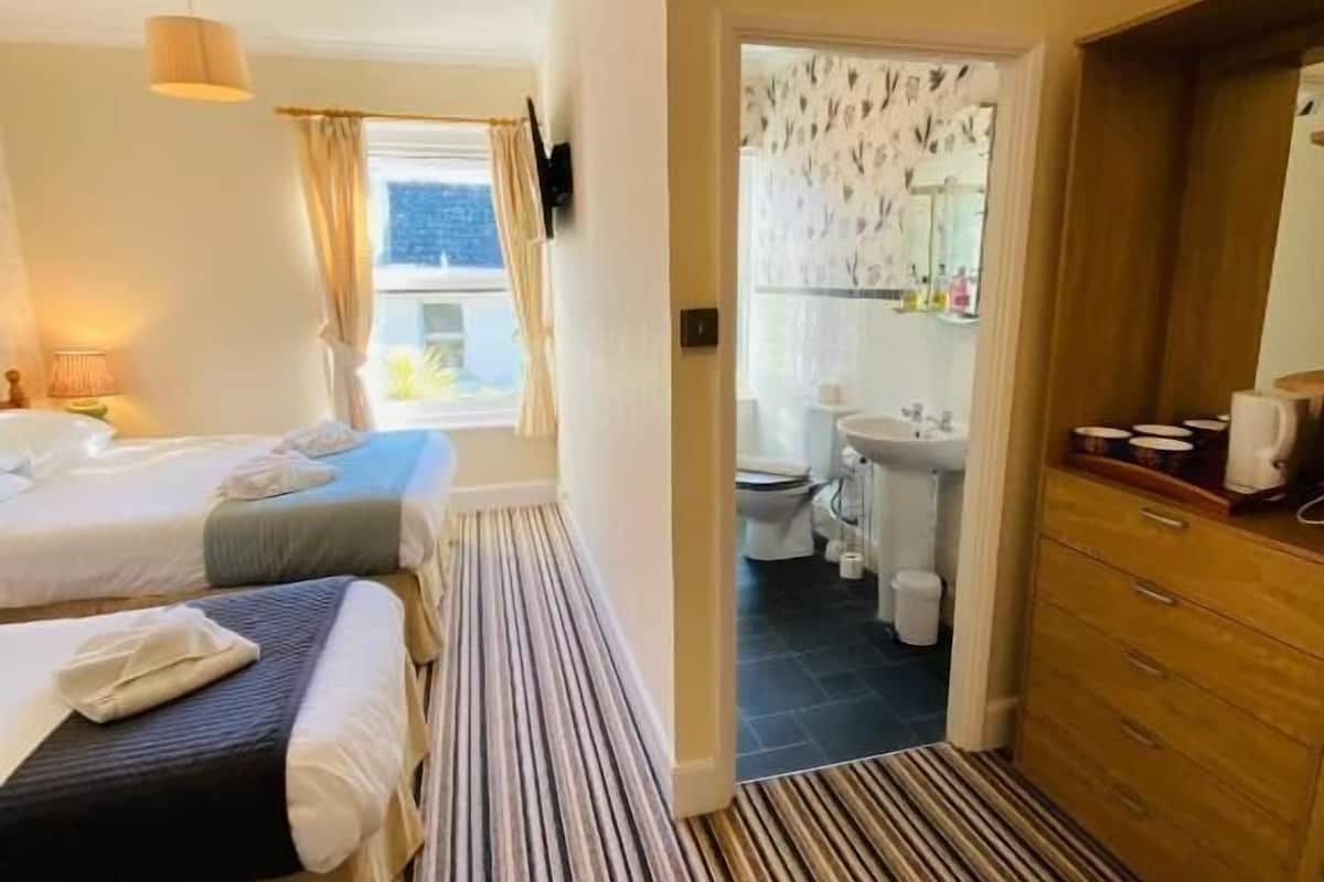 A hotel room with two beds, a wooden dresser, a bathroom with a toilet and sink, and a striped carpet.